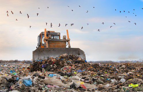 Bulldozer clearing a landfill with birds flying above