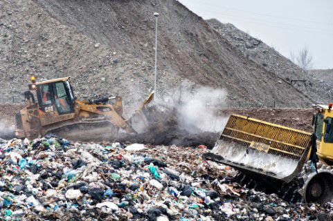 Two bulldozers compacting trash in a landfill